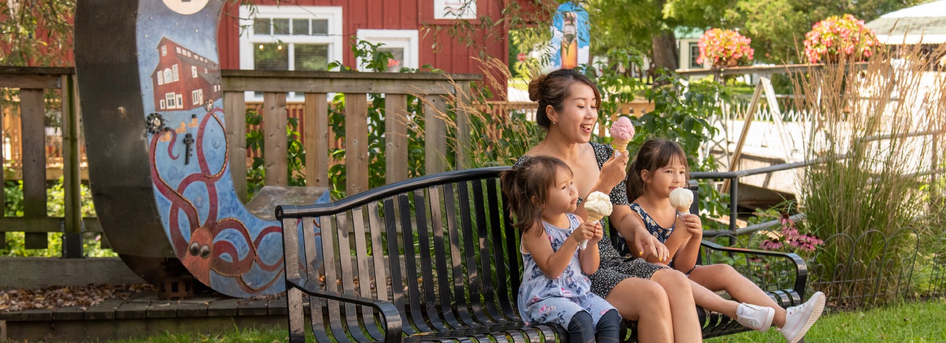 children and woman eating ice cream on a bench