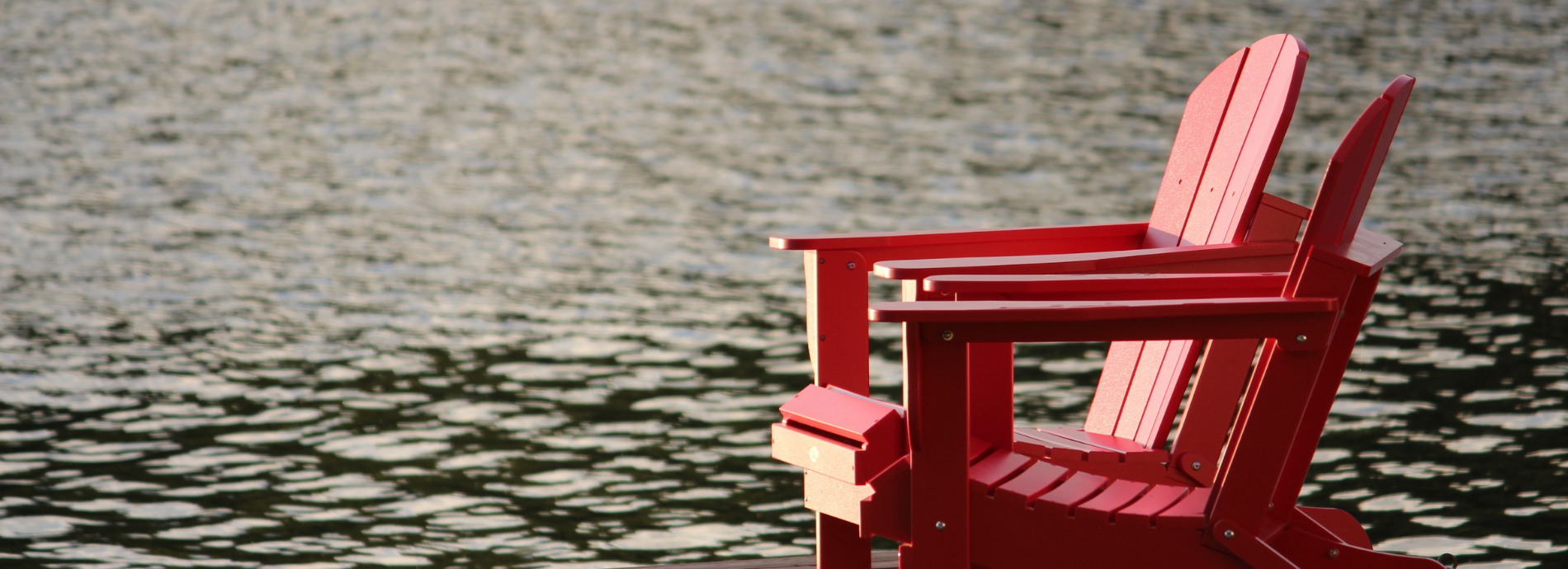 red Muskoka chair on dock by calm lake