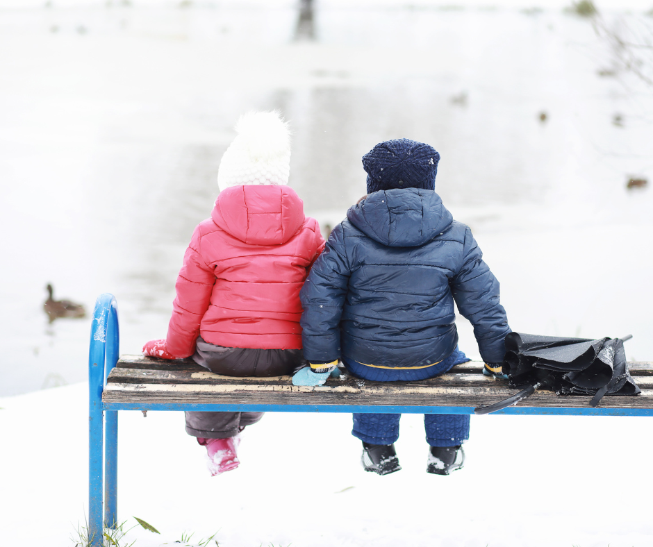 children sitting on a bench near the lake in winter