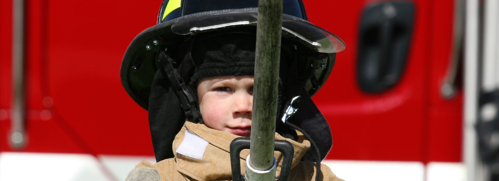 Child in firefighter gear standing in front of a fire truck