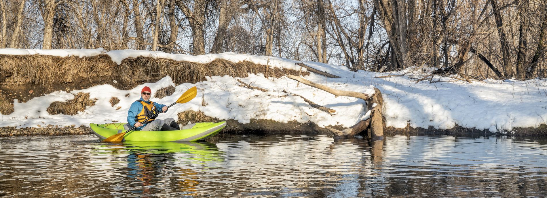 man paddling a kayak in a river during winter